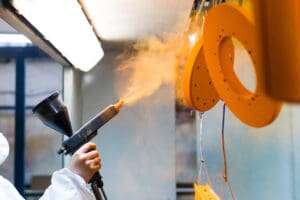 Powder coating of metal parts. A man in a protective suit sprays powder paint from a gun on metal products.